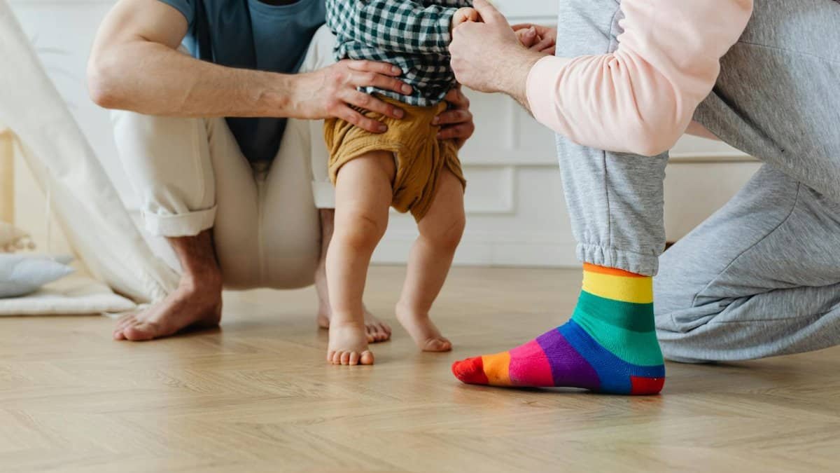 Two parents helping their toddler take first steps in a warm indoor setting, symbolizing love and support.