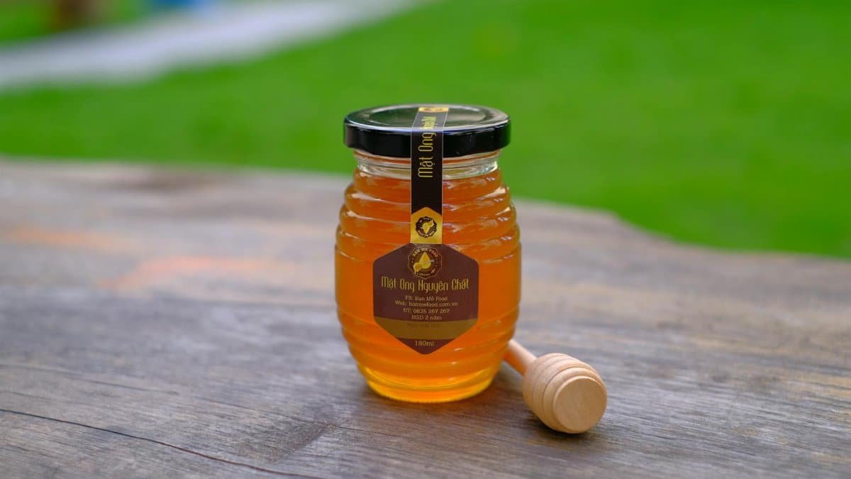 A glass jar of honey with a dipper on a rustic wooden table outdoors.