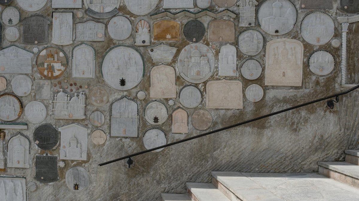 Stone wall adorned with diverse religious relief art panels and stone steps in daylight.
