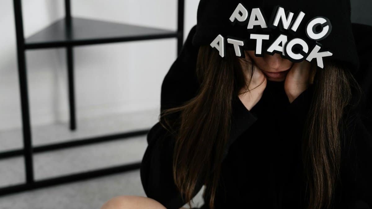A woman sitting with 'PANIC ATTACK' on her hood, showing anxiety indoors.