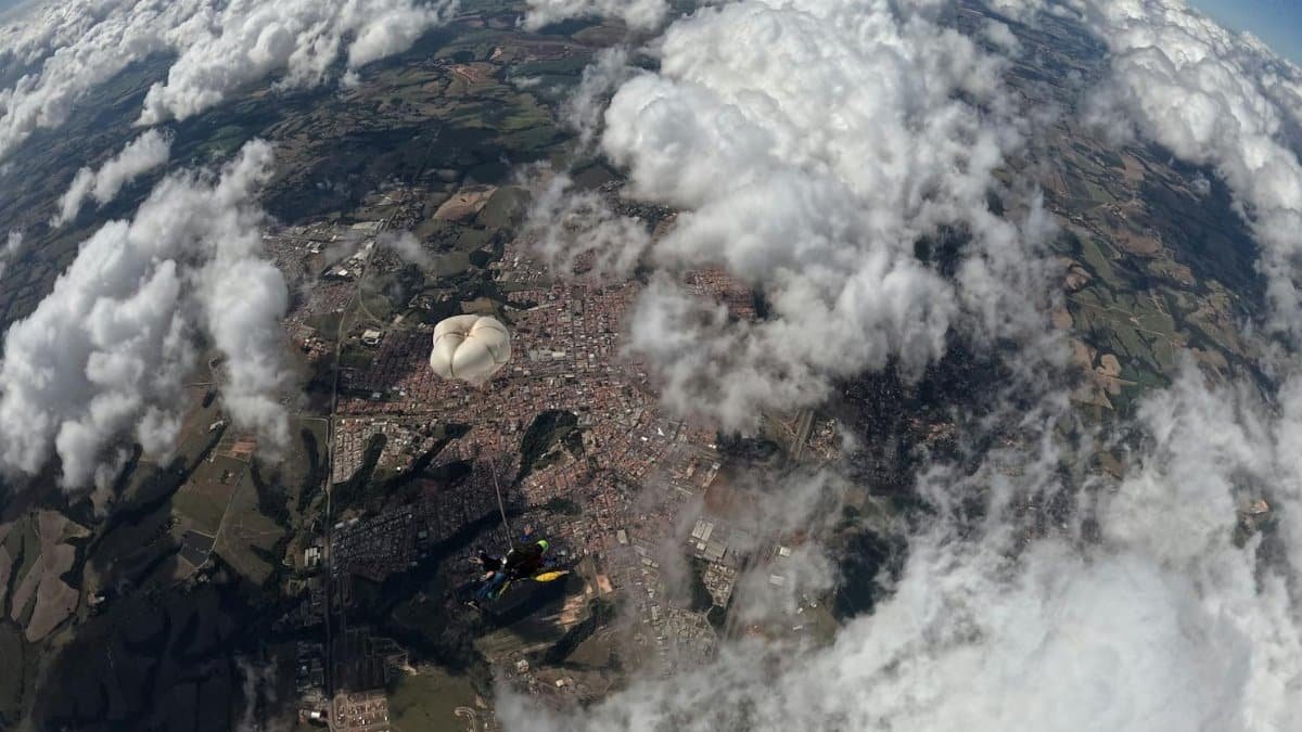 A skydiver floats with a parachute above a sprawling urban landscape beneath clouds.