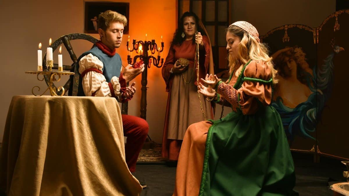 A captivating indoor scene of actors in Renaissance costumes performing on stage, lit by candlelight.