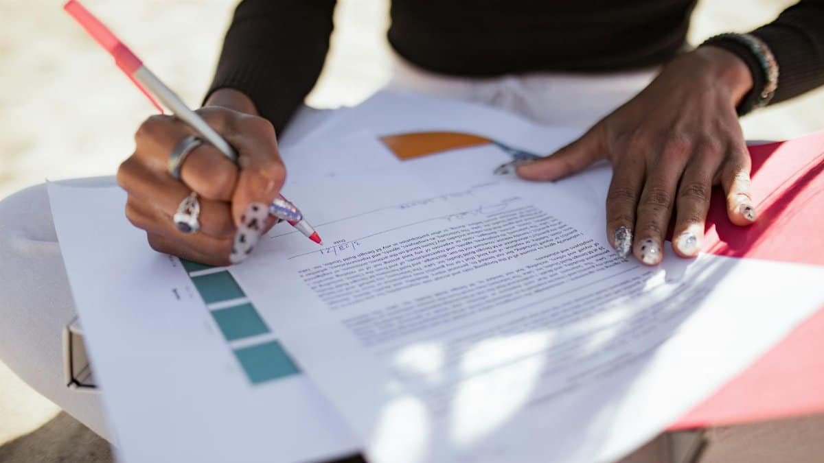 A close-up shows a person editing papers outdoors using a red pen, hinting at a creative review process.