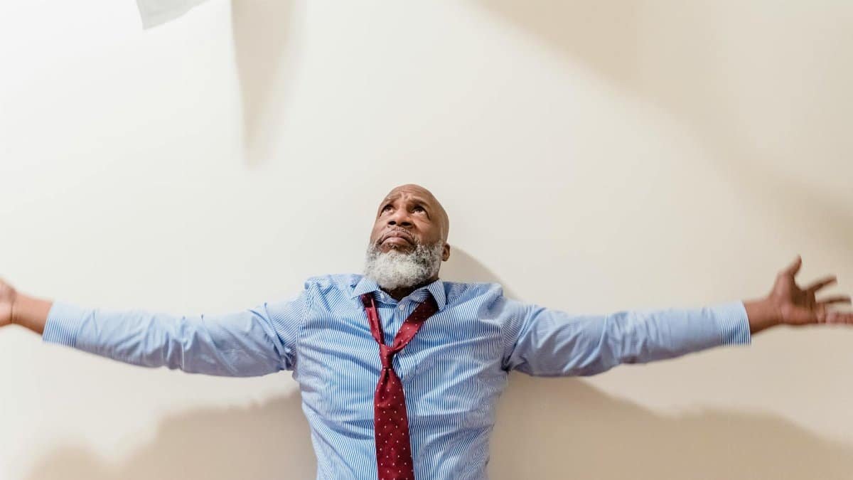 A frustrated businessman with arms outstretched, expressing vulnerability and stress indoors.