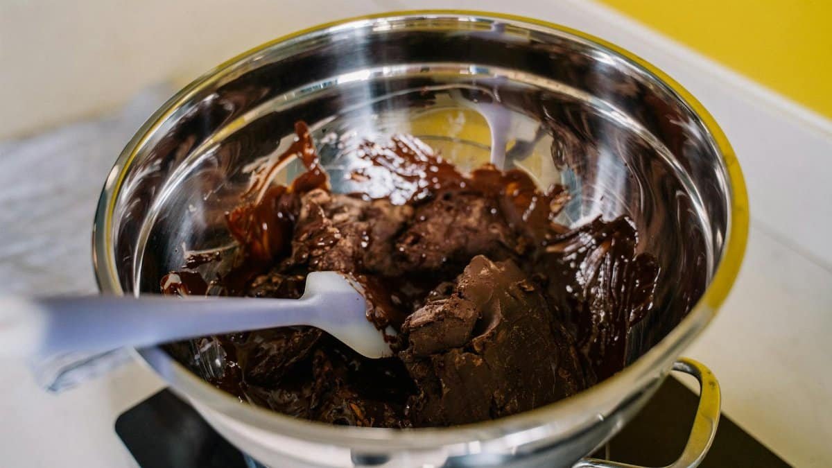Delicious chocolate melting in a stainless steel bowl over a stove with a spatula.
