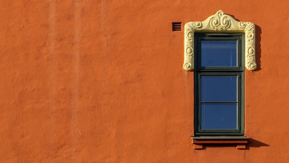 A detailed view of an ornate window set in an orange stucco wall, showcasing rustic architecture.