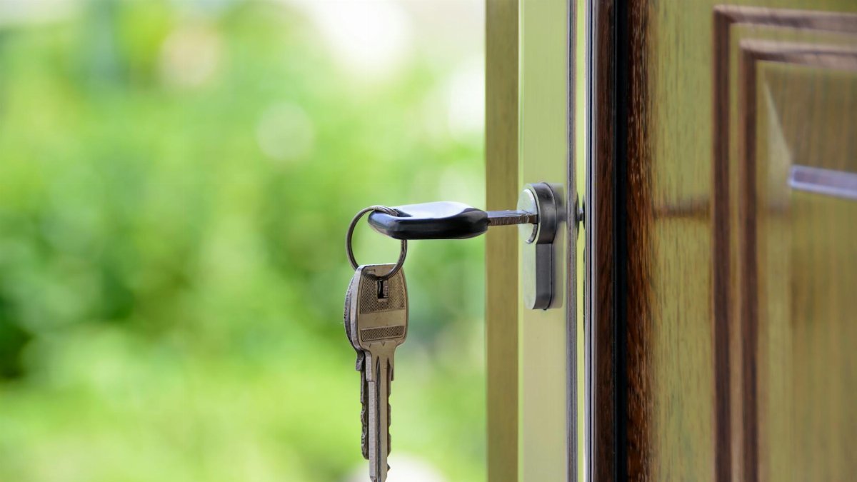 Key inserted in door lock against a blurred green background, symbolizing security and real estate.