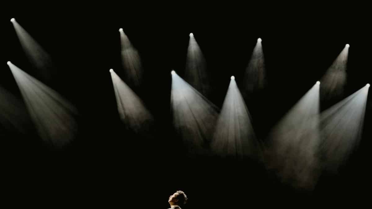 A solo performer stands in a spotlight on a dark stage during a dramatic moment.