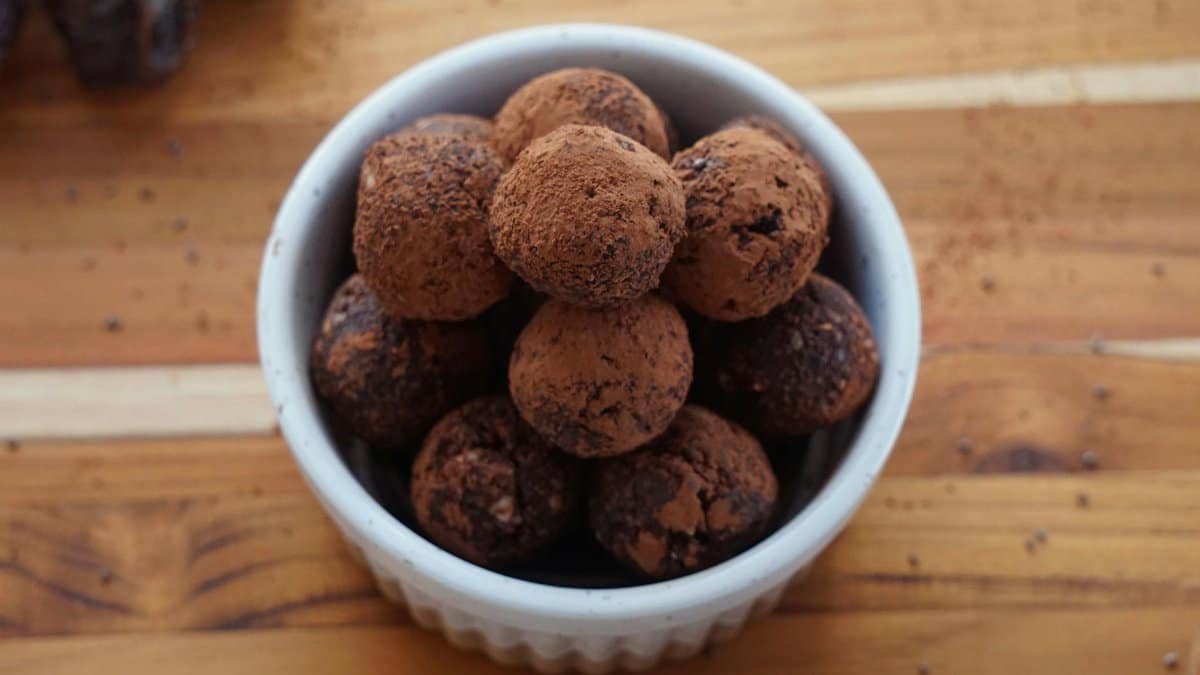 A bowl of homemade chocolate truffles dusted with cacao powder on a rustic wooden surface.