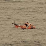 An aerial view of a rescue helicopter flying over the vast ocean, captured mid-flight.