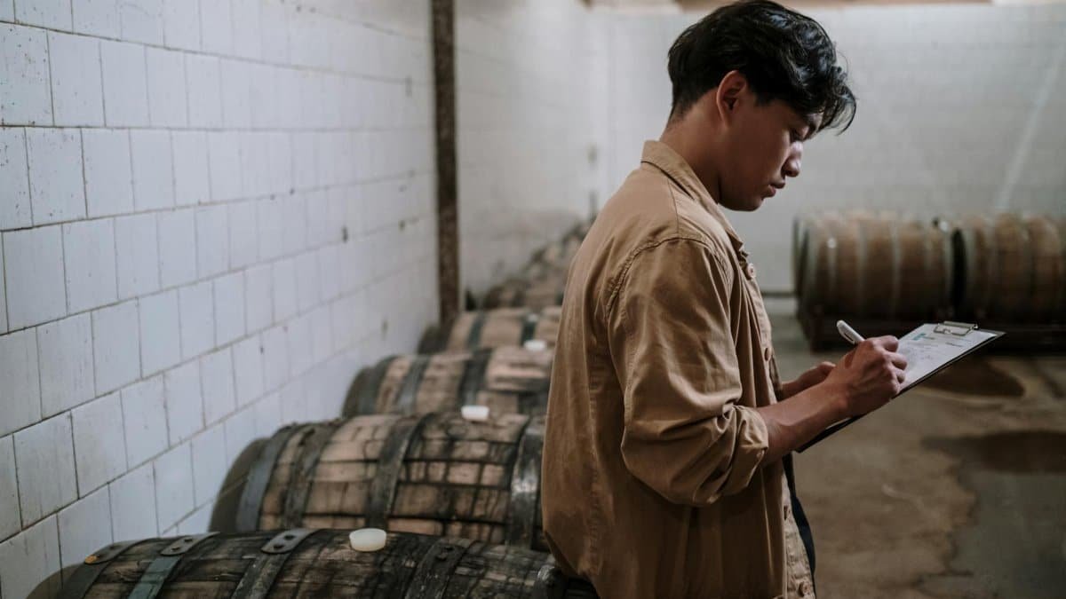 A craft beer expert inspects wooden barrels in a brewery's storage room.