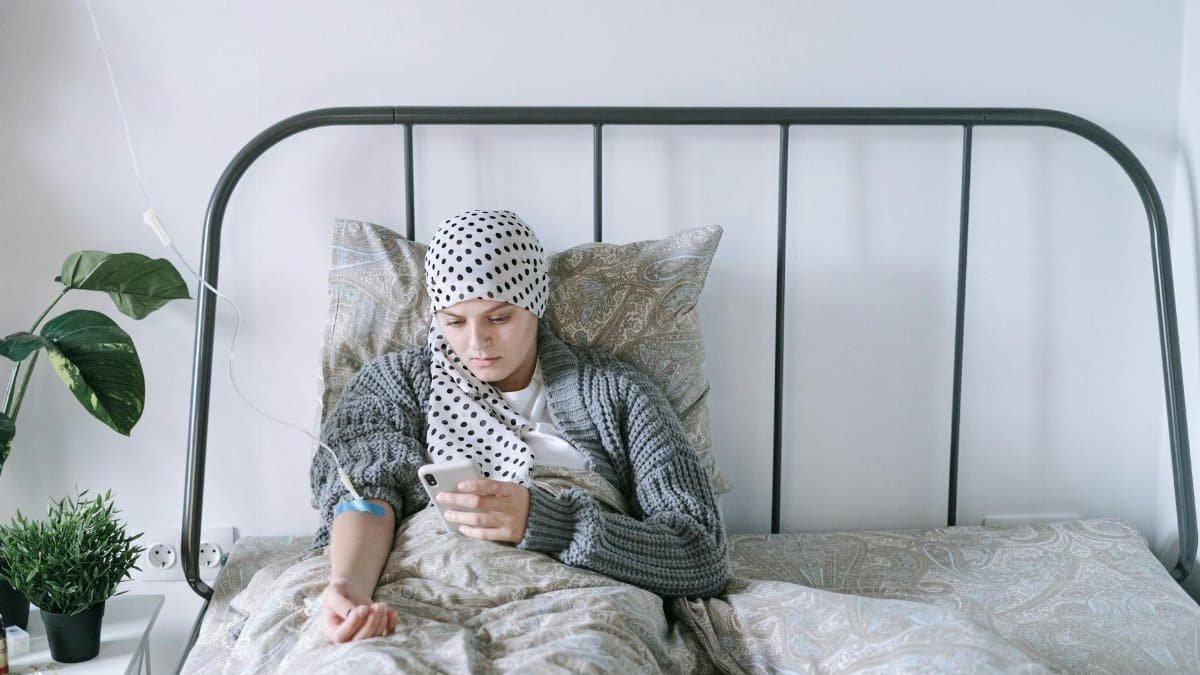 A woman undergoing chemotherapy checks her smartphone in a hospital bed, symbolizing hope and recovery.