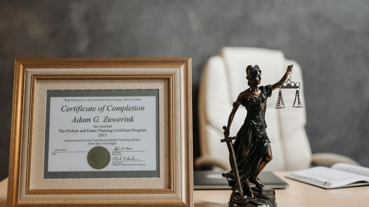 A framed legal certificate and Lady Justice figurine on a desk in a law office setting.