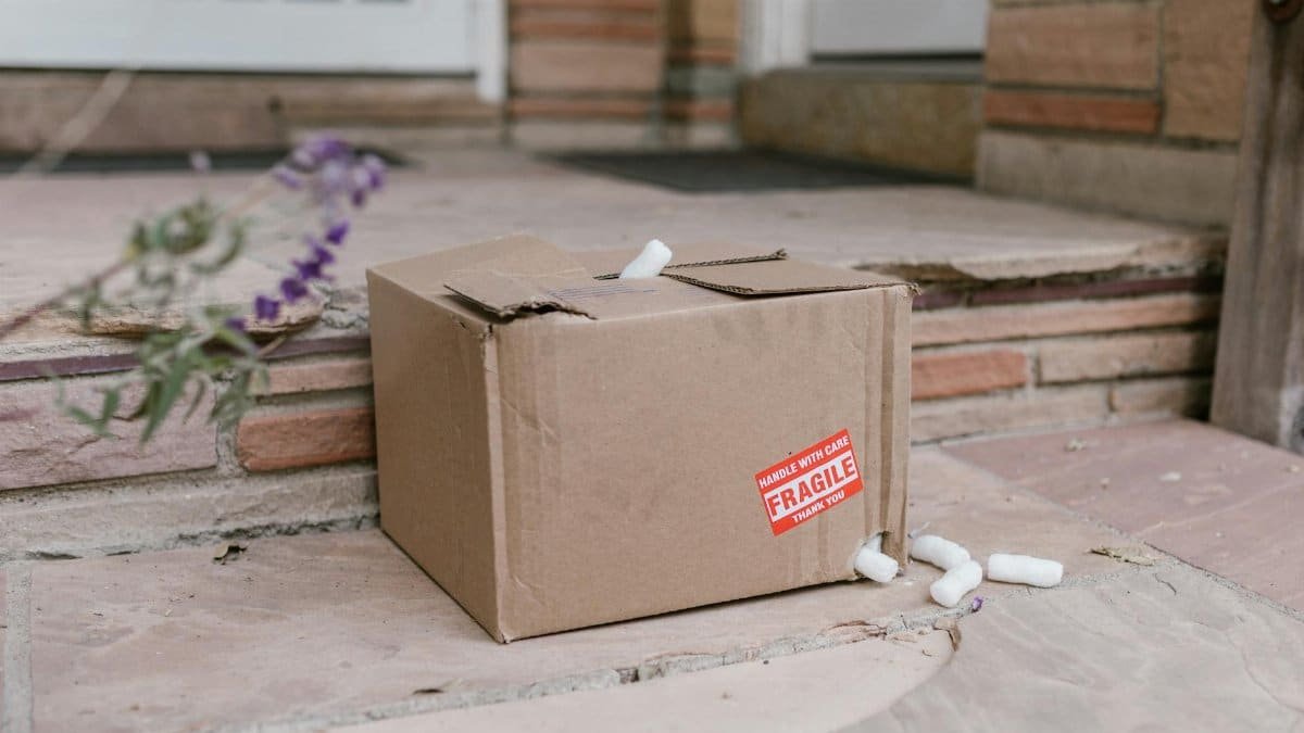 Damaged cardboard package with fragile sticker on porch steps with foam peanuts.