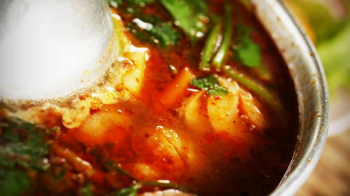Close-up of flavorful Thai Tom Yum soup with aromatic herbs in a metal bowl.