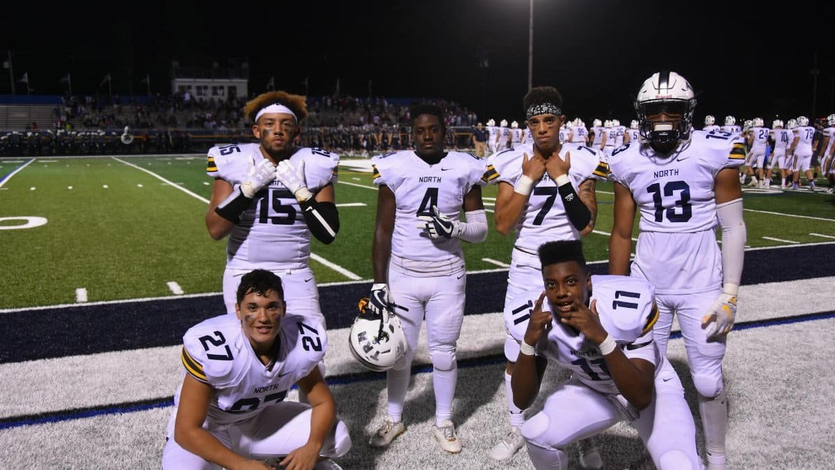 A group of high school football players posing on the field at night, wearing uniforms.