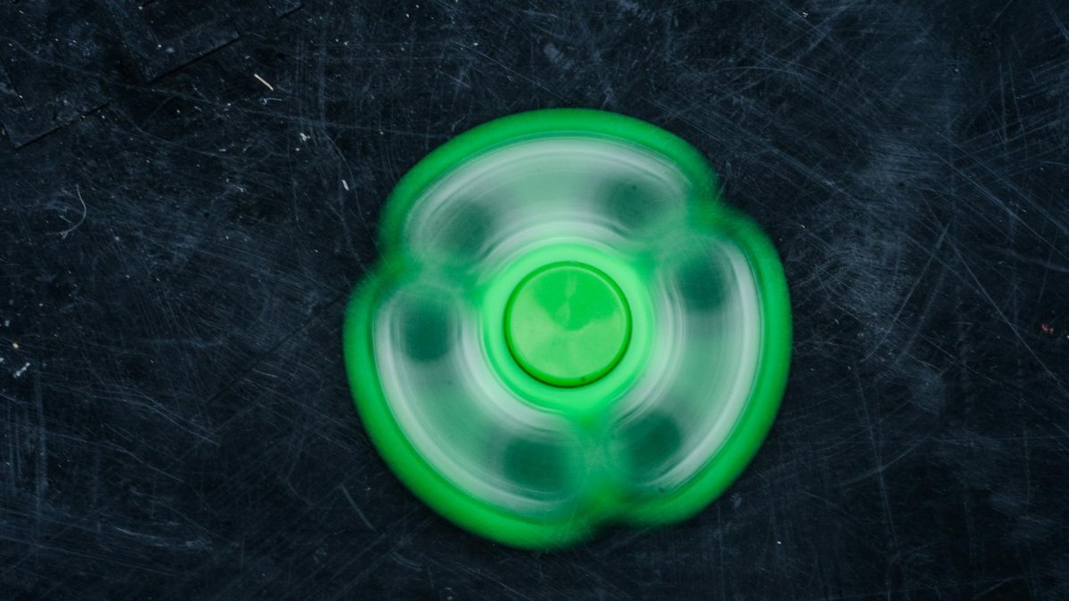 A vibrant green fidget spinner spinning rapidly against a dark textured background.