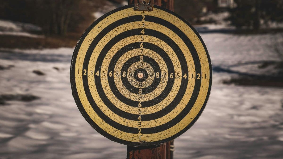 Yellow target for shooting with black circles and numbers on wooden post in countryside with snowy ground on winter day