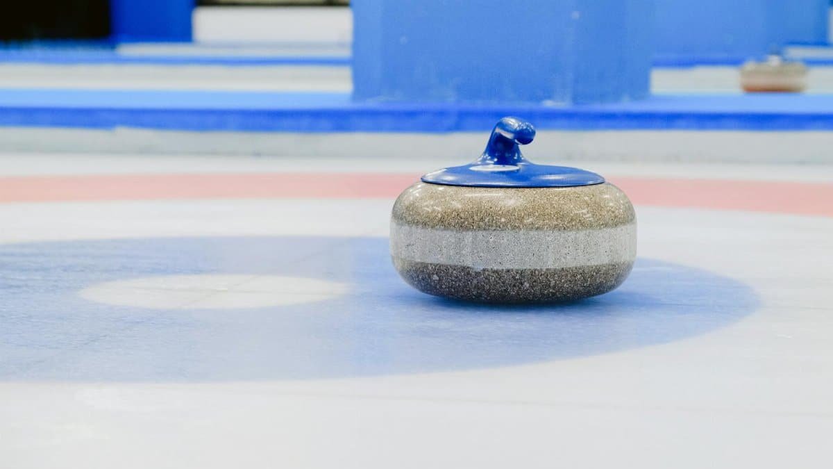 A close-up view of a curling stone on a vibrant indoor ice rink with colorful circles.