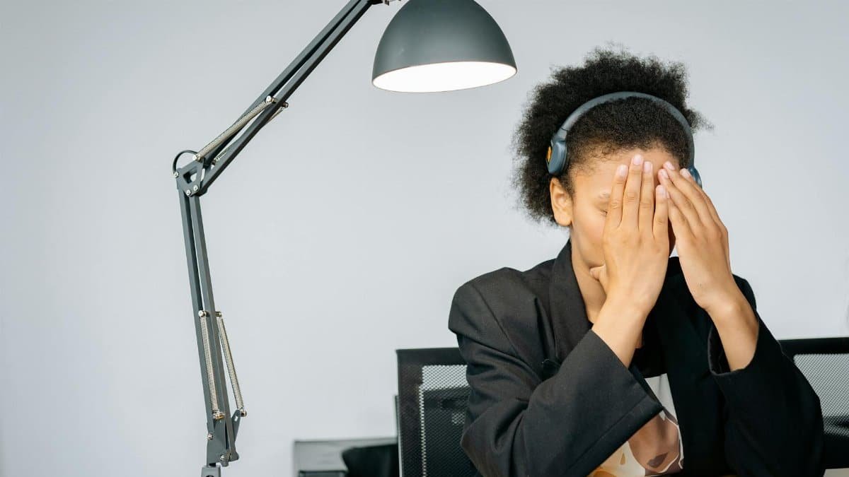 Overworked call center agent with hands on face, feeling exhausted while working in the office.