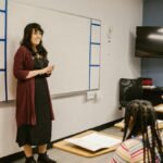A teacher conducts a lesson with attentive diverse students in a modern classroom setting.