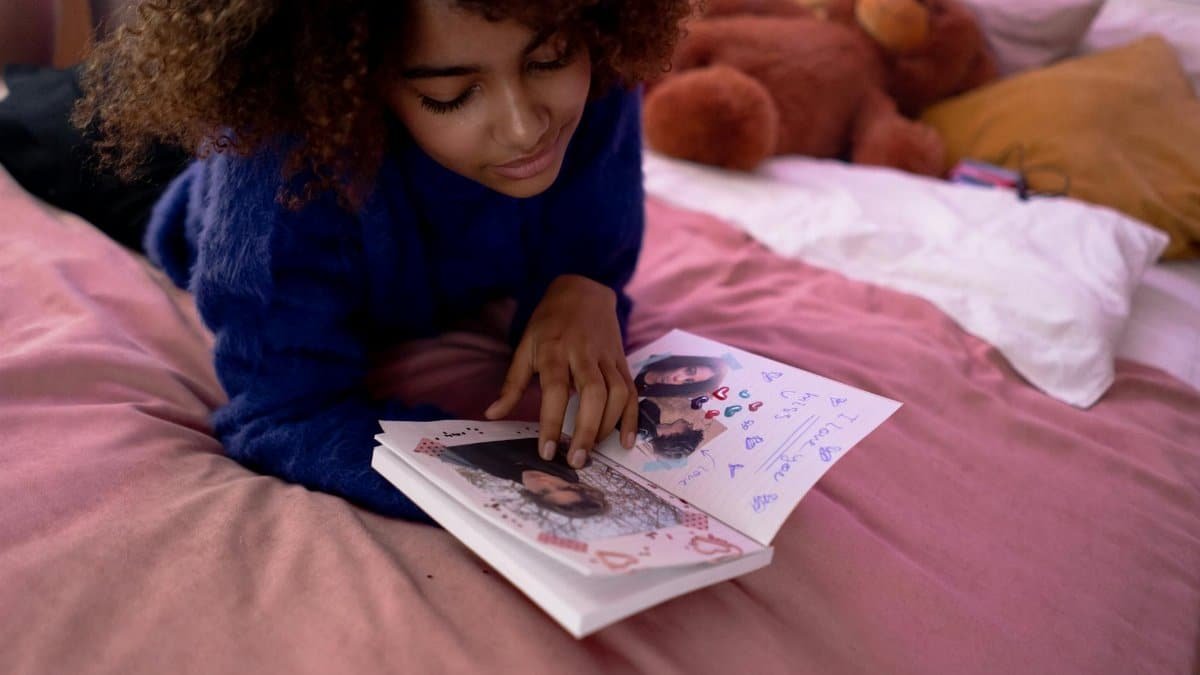 Teen girl relaxes on her bed, reading a personalized diary with a stuffed teddy bear.