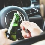 Hands opening a beer bottle inside a car, highlighting the importance of safe driving and awareness of road dangers.