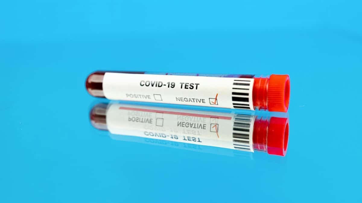 A test tube with negative COVID-19 results on a reflective blue surface.