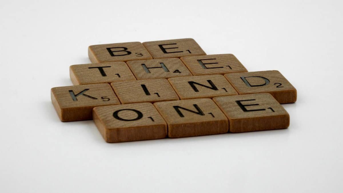 Wooden Scrabble tiles spelling 'Be The Kind One' with focus on words and white background.