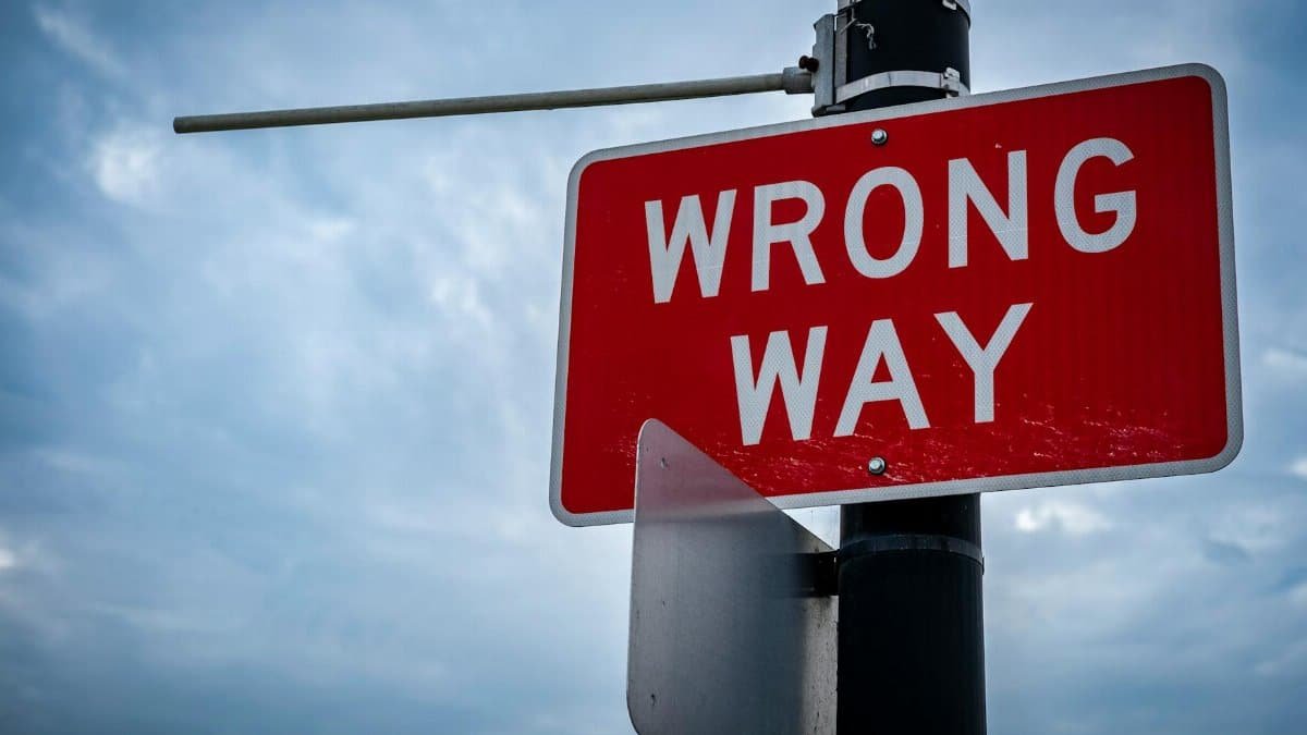 A close-up of a red wrong way road sign against an overcast sky, symbolizing caution.