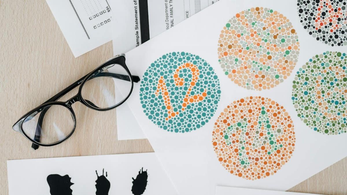 Close-up of color blindness test sheets with eyeglasses on a wooden table.