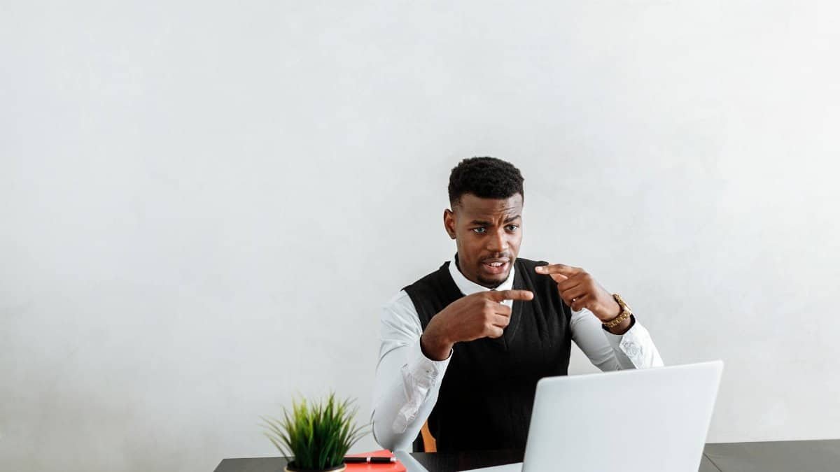 Professional businessman explaining during video call using laptop in modern office setting.