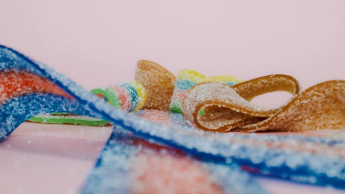 Vibrant macro shot of sugary sour candy ribbons on a pink background.