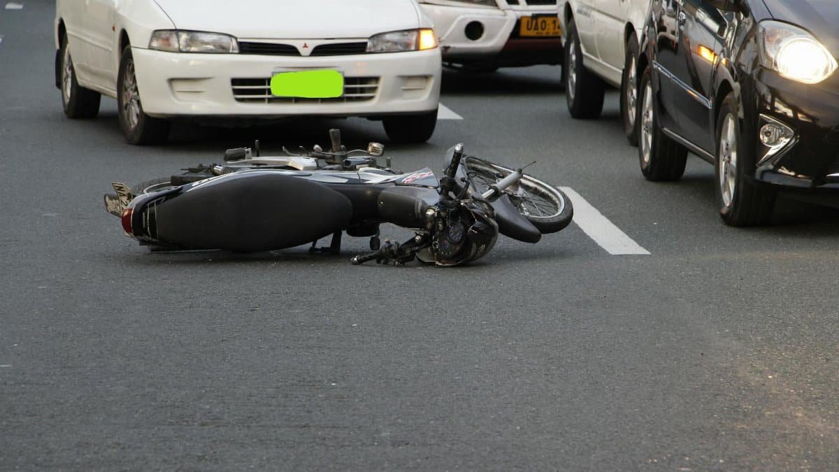 A motorcycle lies on a city road amidst traffic, indicating a recent accident.