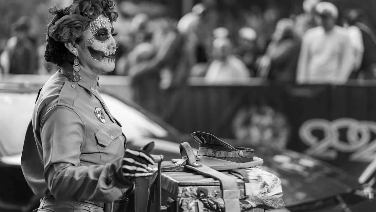 Monochrome photo of a Catrina with elaborate skull makeup and floral headdress in a Mexico City parade.