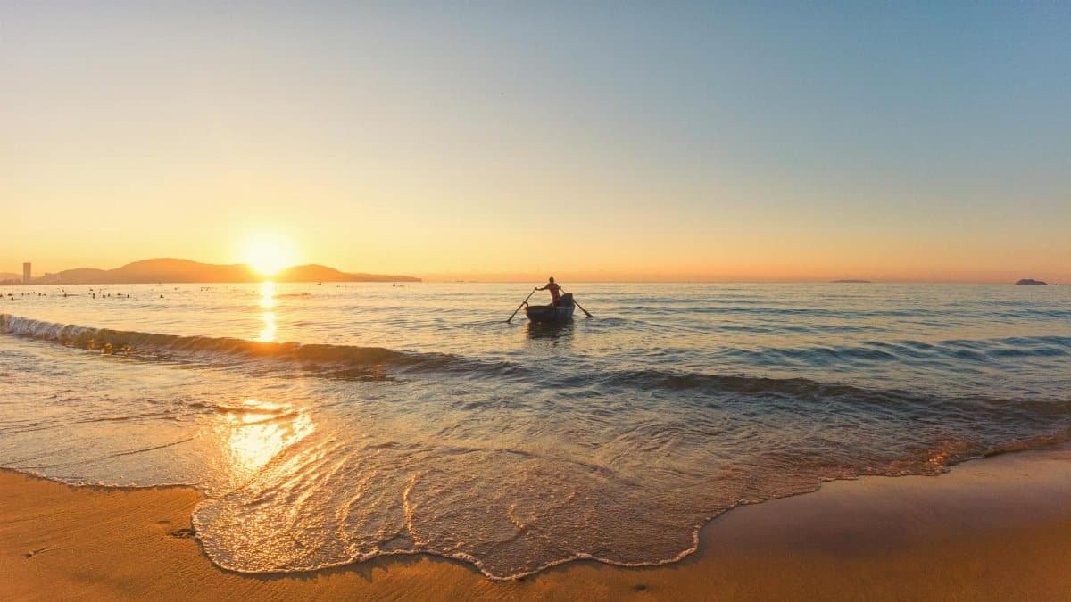 A serene scene of a lone fisherman rowing at sunrise on Quy Nhơn beach, Bình Định, Vietnam.