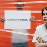 A worried person standing in front of a transparent barrier with 'Coronavirus' sign, illustrating pandemic anxiety.