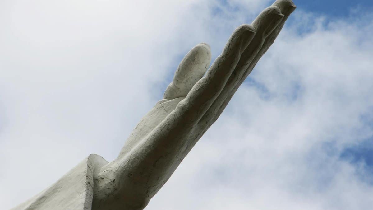 A low angle view of the hand of the Cristo Rey statue in Cali, Colombia against a blue sky with clouds.