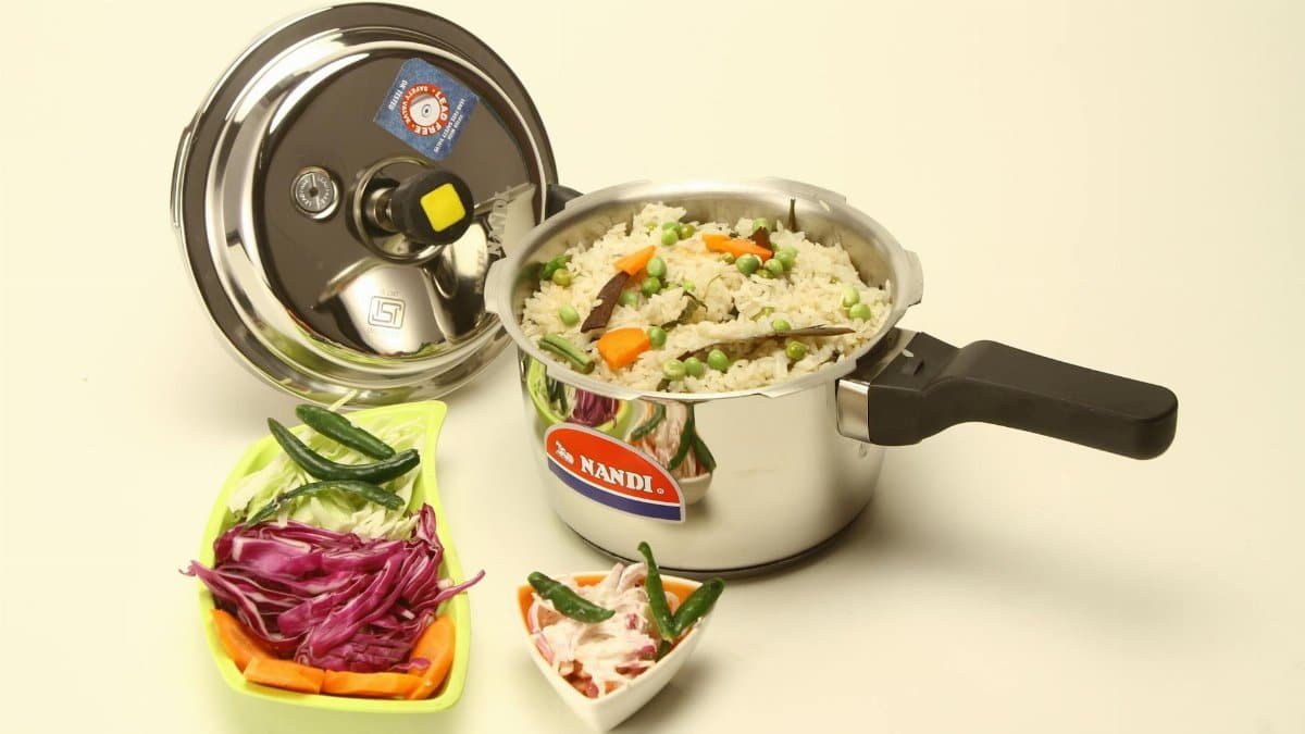 Metal pressure cooker with Indian vegetable rice, side salads, and spices in a studio setting.