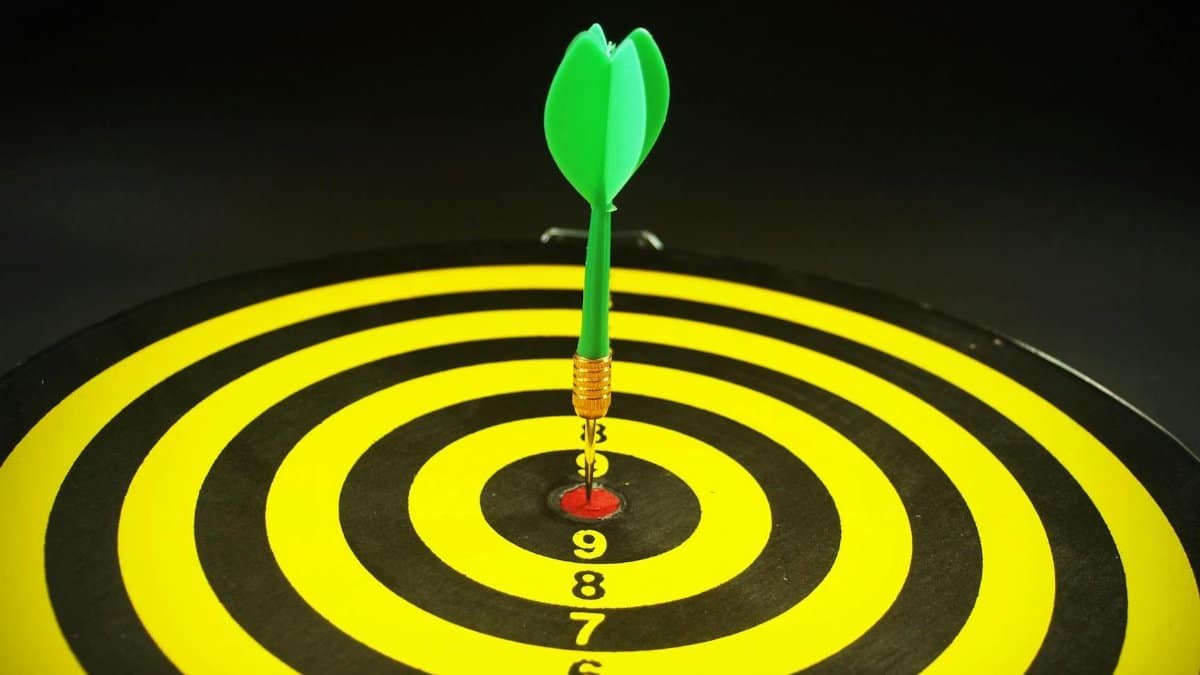 Close-up of a green dart hitting the bullseye on a yellow and black target board, symbolizing precision and success.