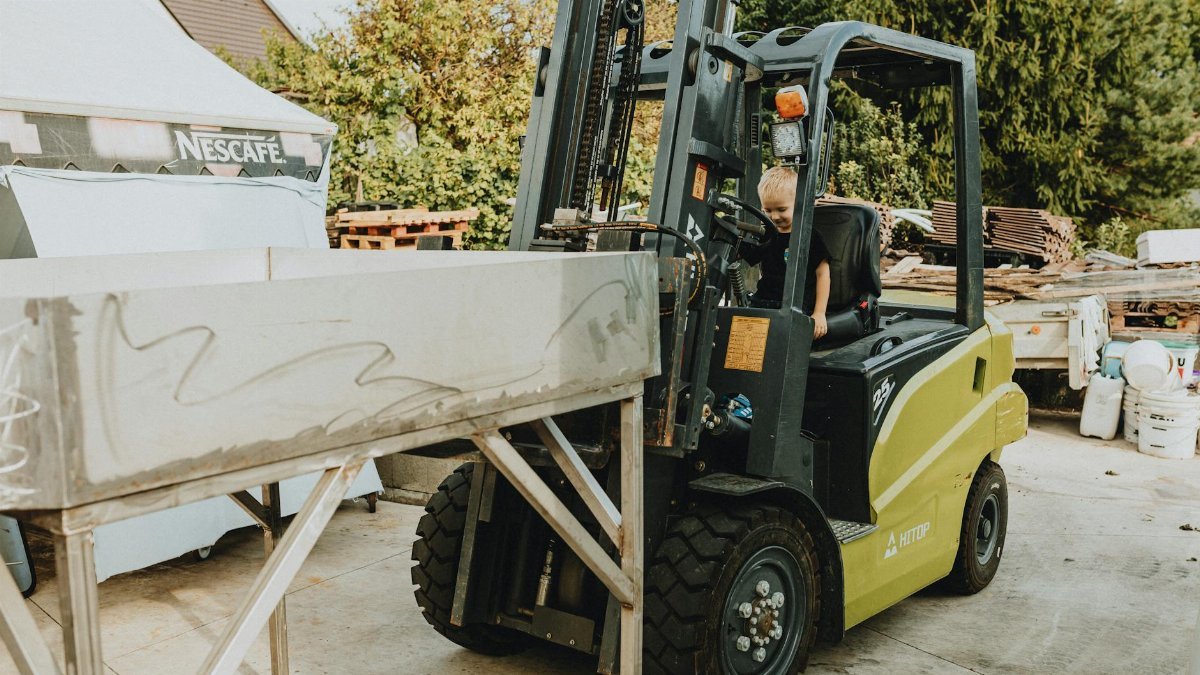 A young child sitting inside a forklift in an outdoor workshop setting, showcasing curiosity and play.
