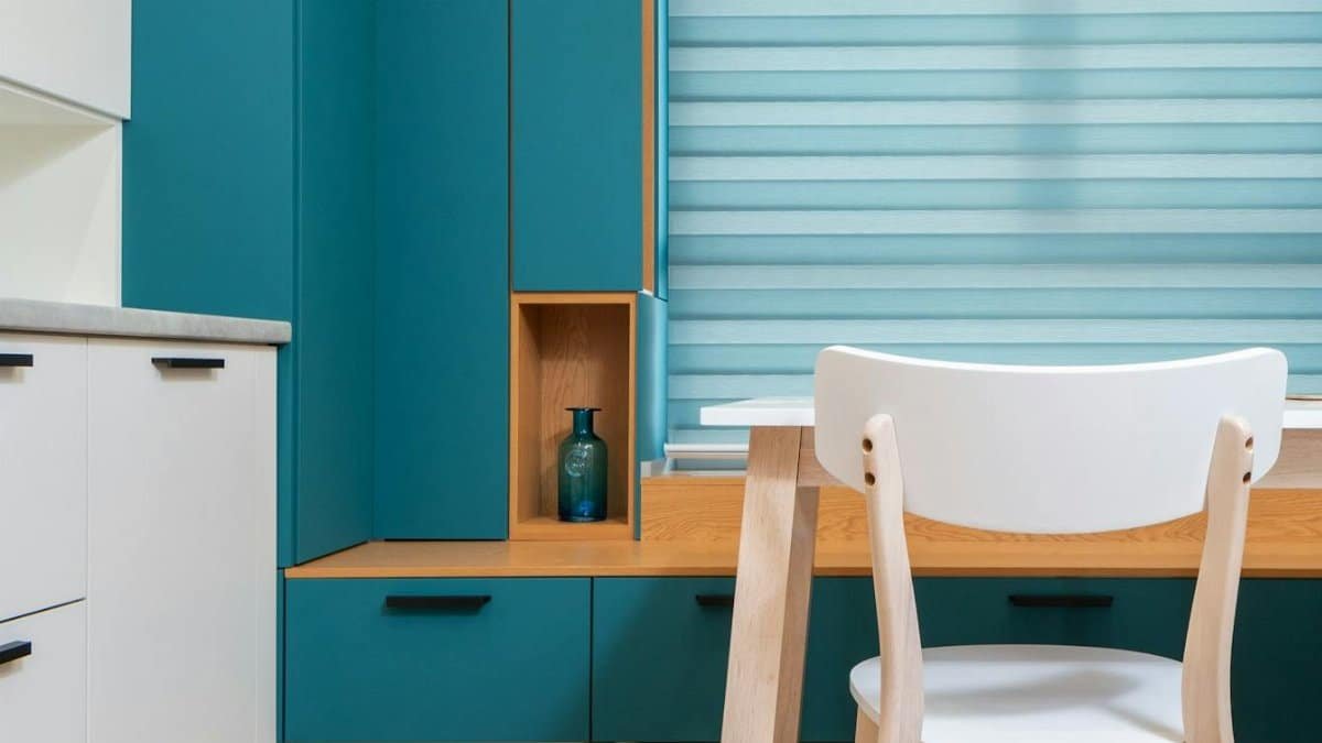 Modern kitchen interior with decorative vase on shelf of cabinet and window blind against table in house