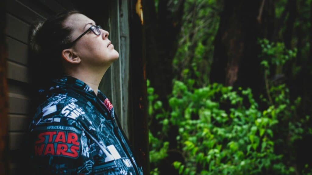 Profile of a woman standing outdoors, wearing a Star Wars jacket, surrounded by greenery.