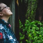 Profile of a woman standing outdoors, wearing a Star Wars jacket, surrounded by greenery.
