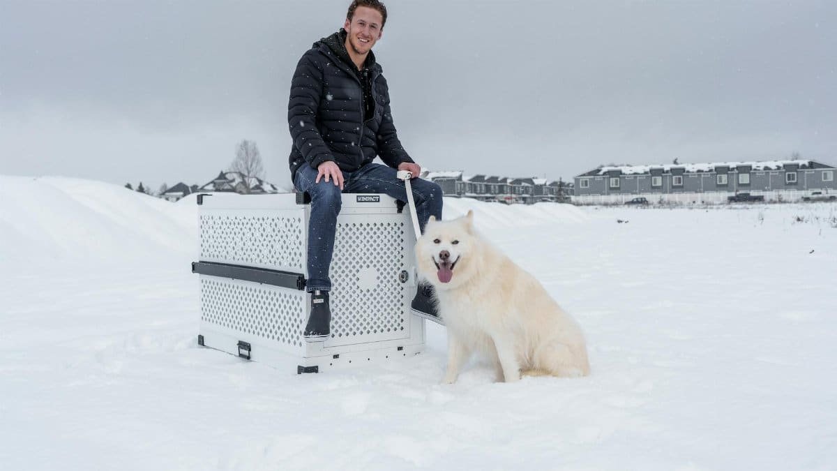 A smiling man with his Siberian Husky dog next to a durable impact dog crate in a snowy outdoor setting.