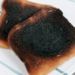 Two slices of burnt toast served on a white ceramic plate, perfect for breakfast or food concepts.