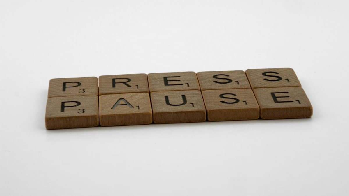 Wooden Scrabble tiles arranged to spell 'Press Pause' on a clean white background.