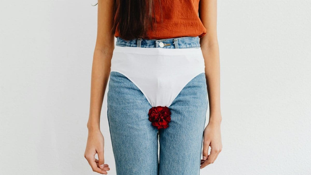 Symbolic representation of menstruation using red flower on jeans, addressing social issues.
