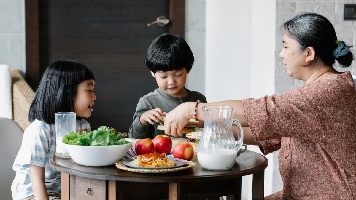 A grandmother and her grandchildren enjoy a healthy meal together. Indoors, warm and happy.