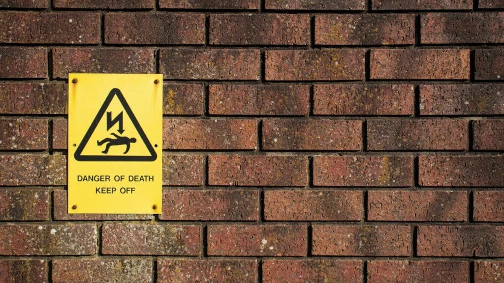 A bold warning sign on a brick wall displaying 'Danger of Death', emphasizing caution.